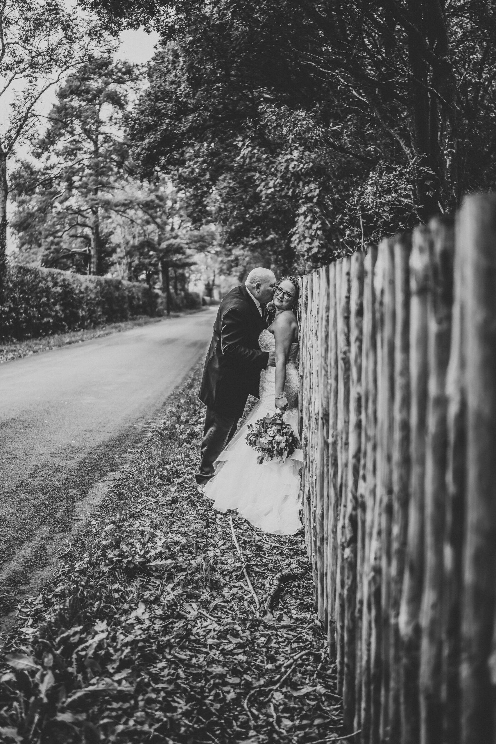 a groom leaning against a wooden fence as he kisses his new wife taken by a hampshire wedding photographer 