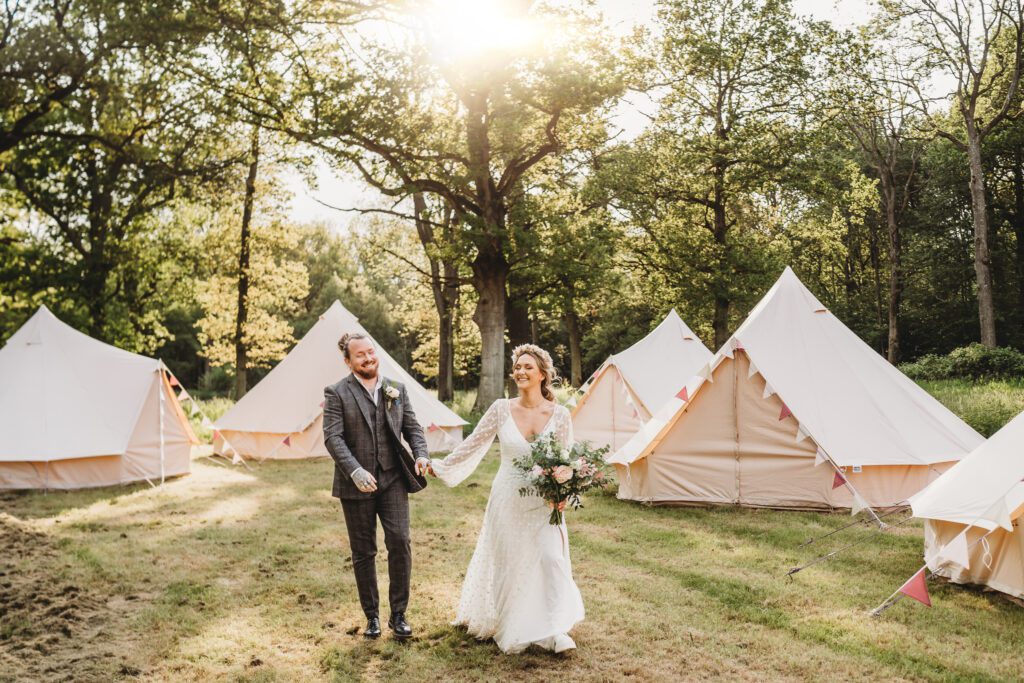 a bride and groom walking hand in hand through bell tents in a festival field 