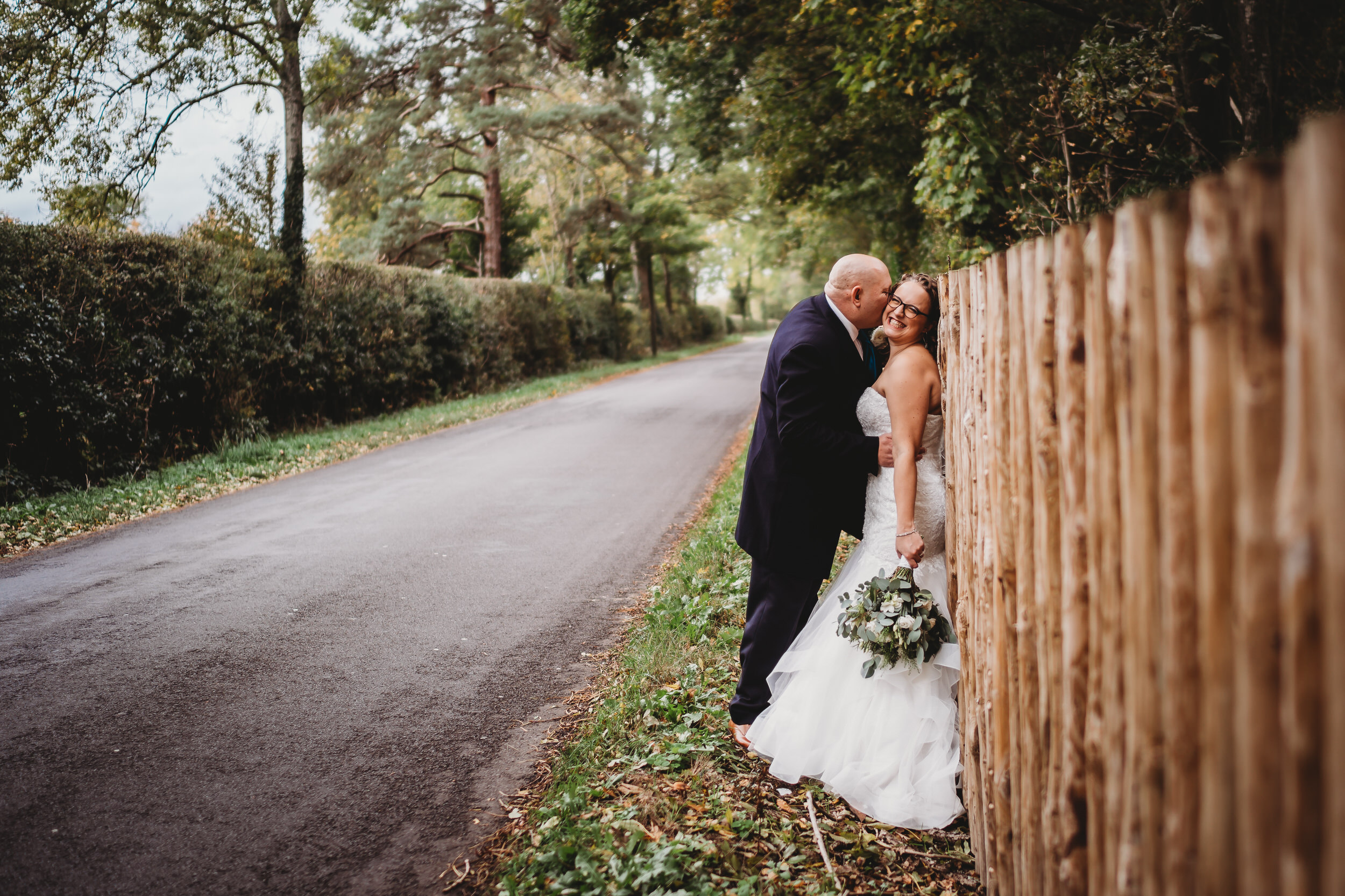 a groom leaning against a wooden fence as he kisses his new wife taken by a hampshire wedding photographer