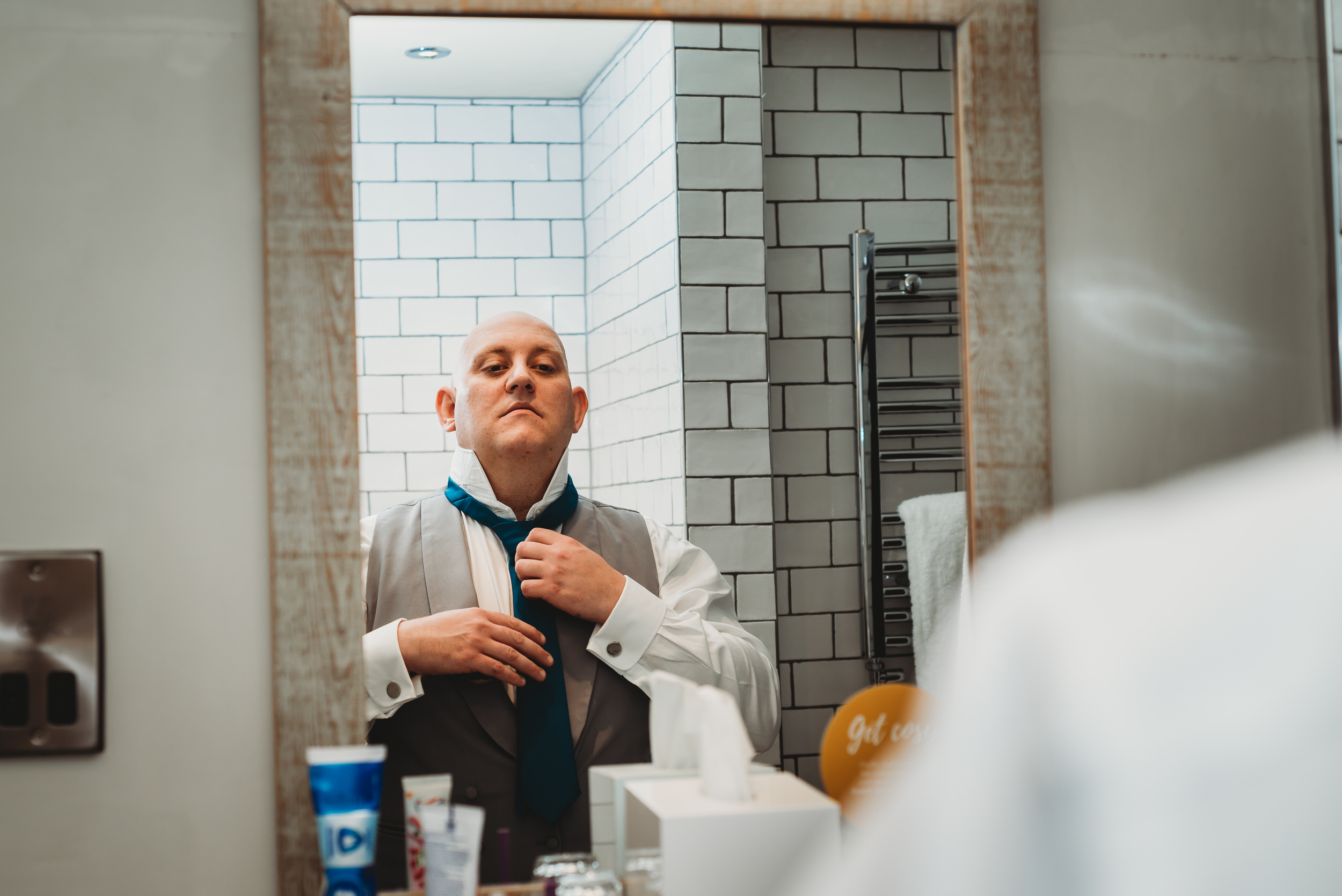 a groom sorting his tie in a bathroom mirror before his wedding
