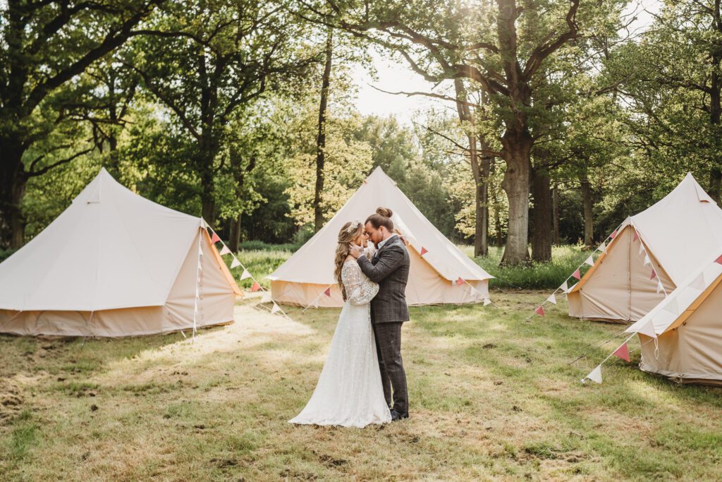 a bride and groom cuddling amongst trees and tents during a festival wedding