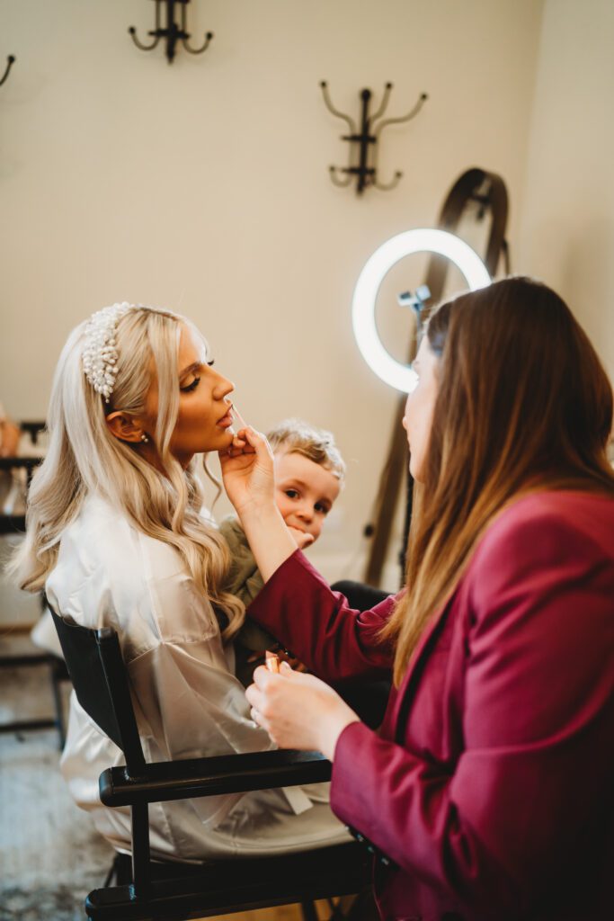 make up artist adding finale touches to the bride before her wedding at the post barn newbury