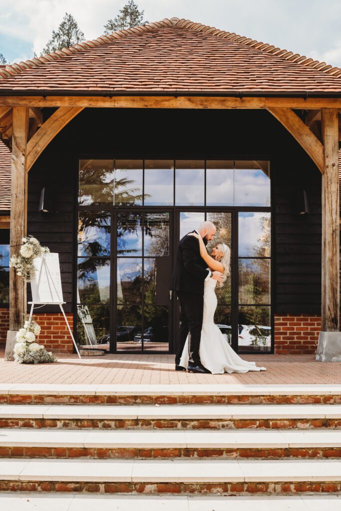 a bride and groom cuddling in front of the post barn newbury