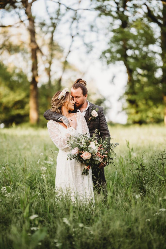 Festival wedding photography of a bride and groom cuddling together in long grasses after their ceremony