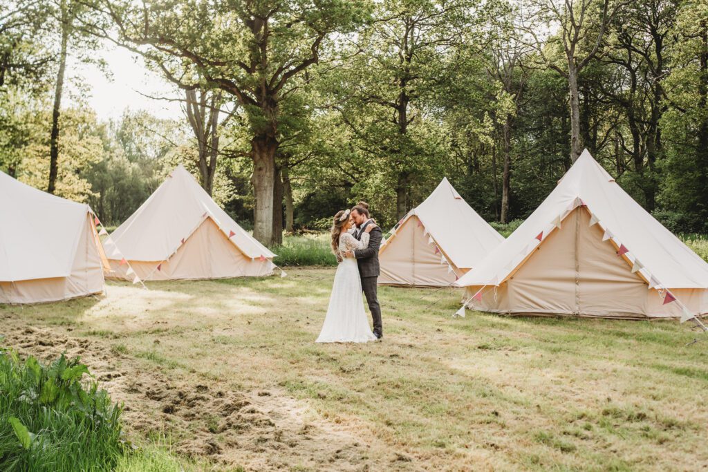 a bride and groom cuddling amongst trees and tents during a festival wedding