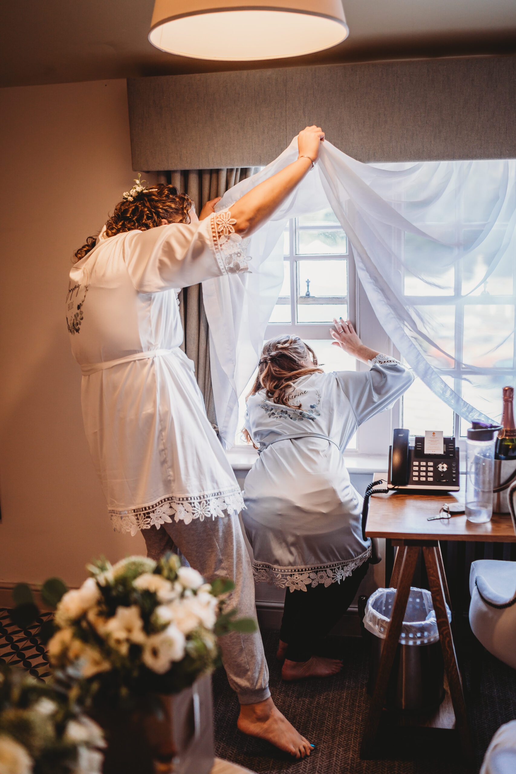 bride and bridesmaid looking out the window at the arriving guests at The wellington Arms in Hampshire