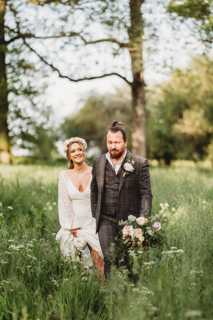 a bride and groom laughing and walking together in long grass taken by a festival wedding photographer 