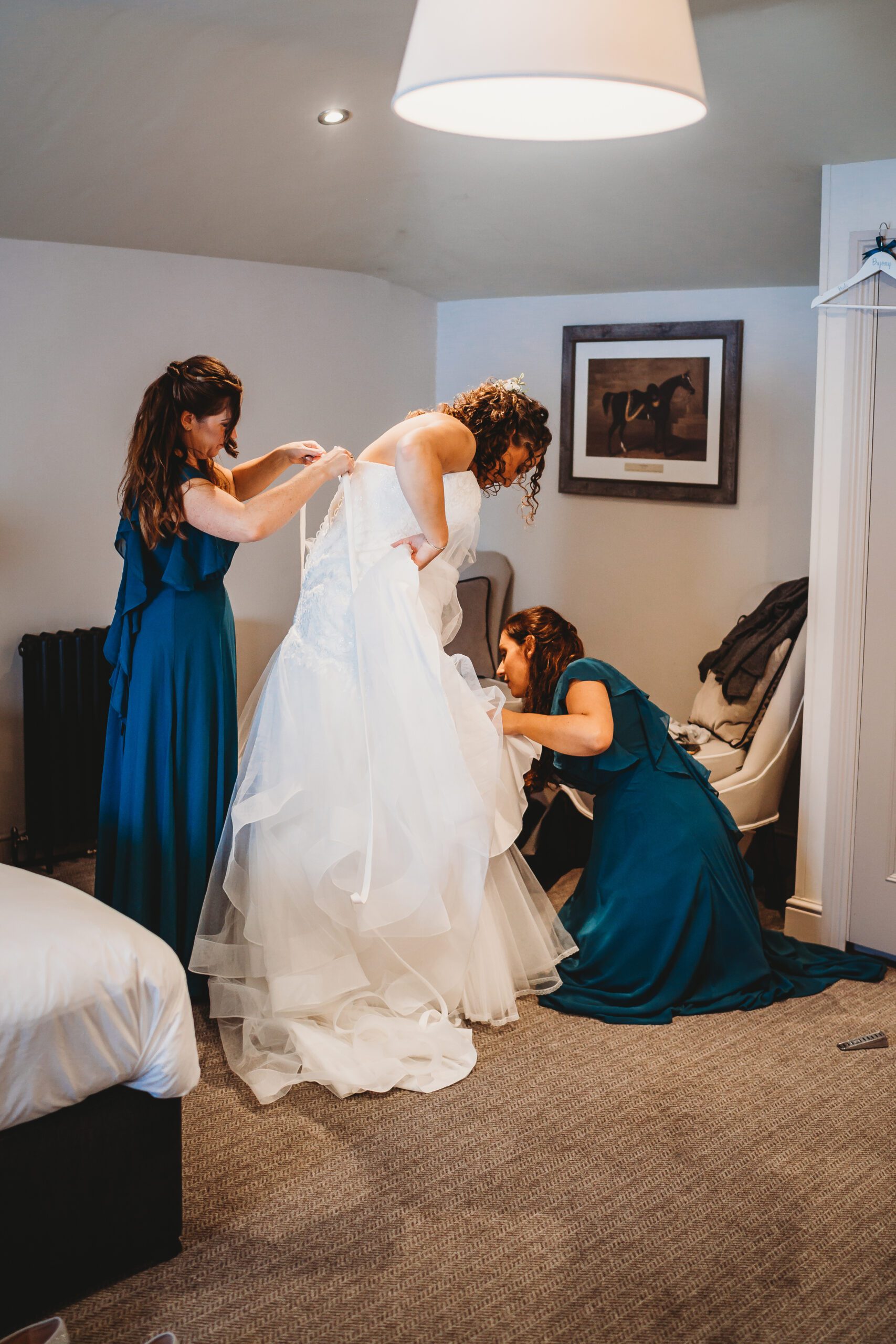 bridesmaids helping the bride get ready as taken by a hampshire wedding photographer