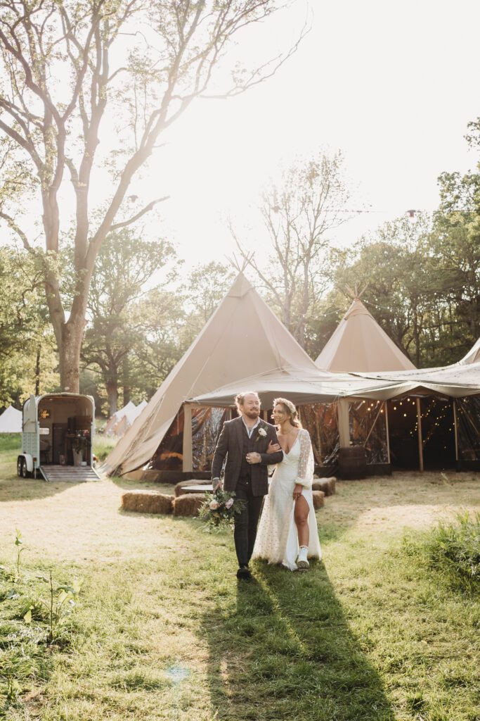 a bride and groom linking arms and walking with the tipis in the background taken by a festival wedding photographer 