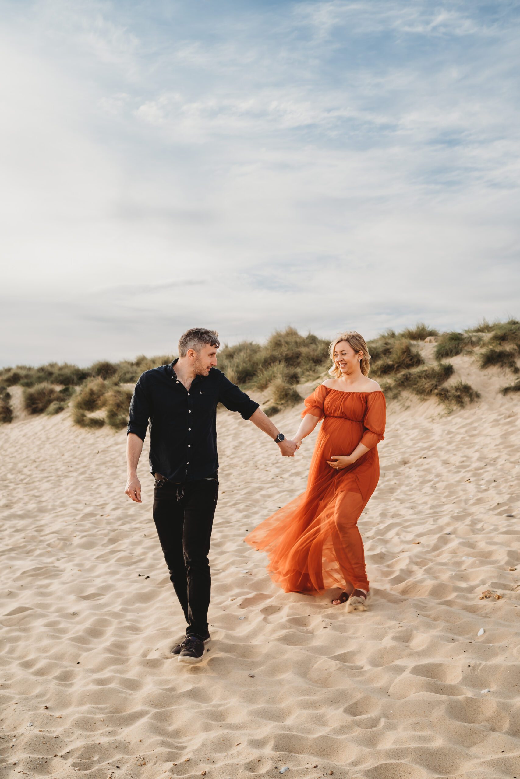 a husband leading his pregnant wife down the sand dunes of hengsitbury beach