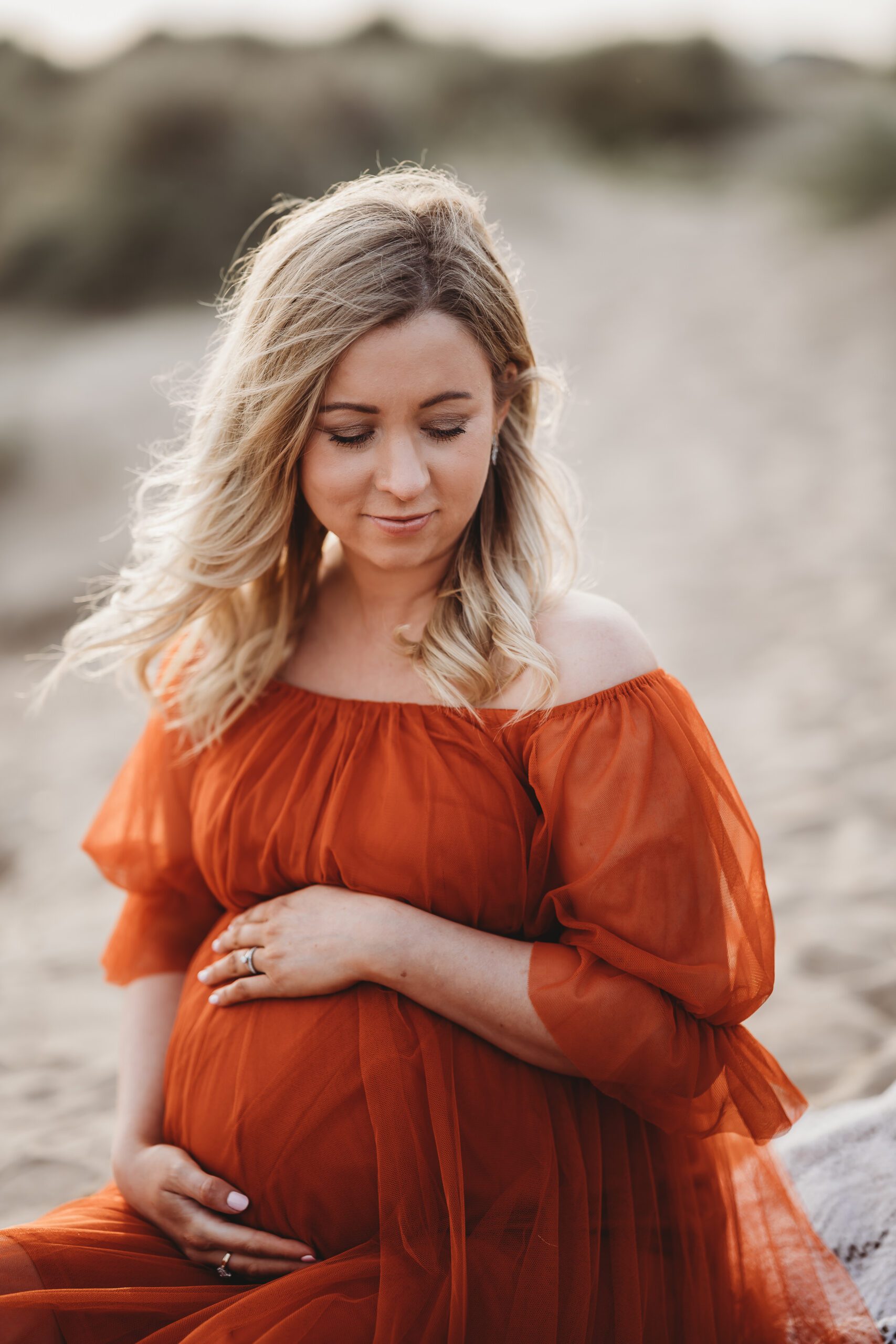 a close up image of a pregnant lady holding on to her bump in a bright orange dress taken by a newbury maternity photographer