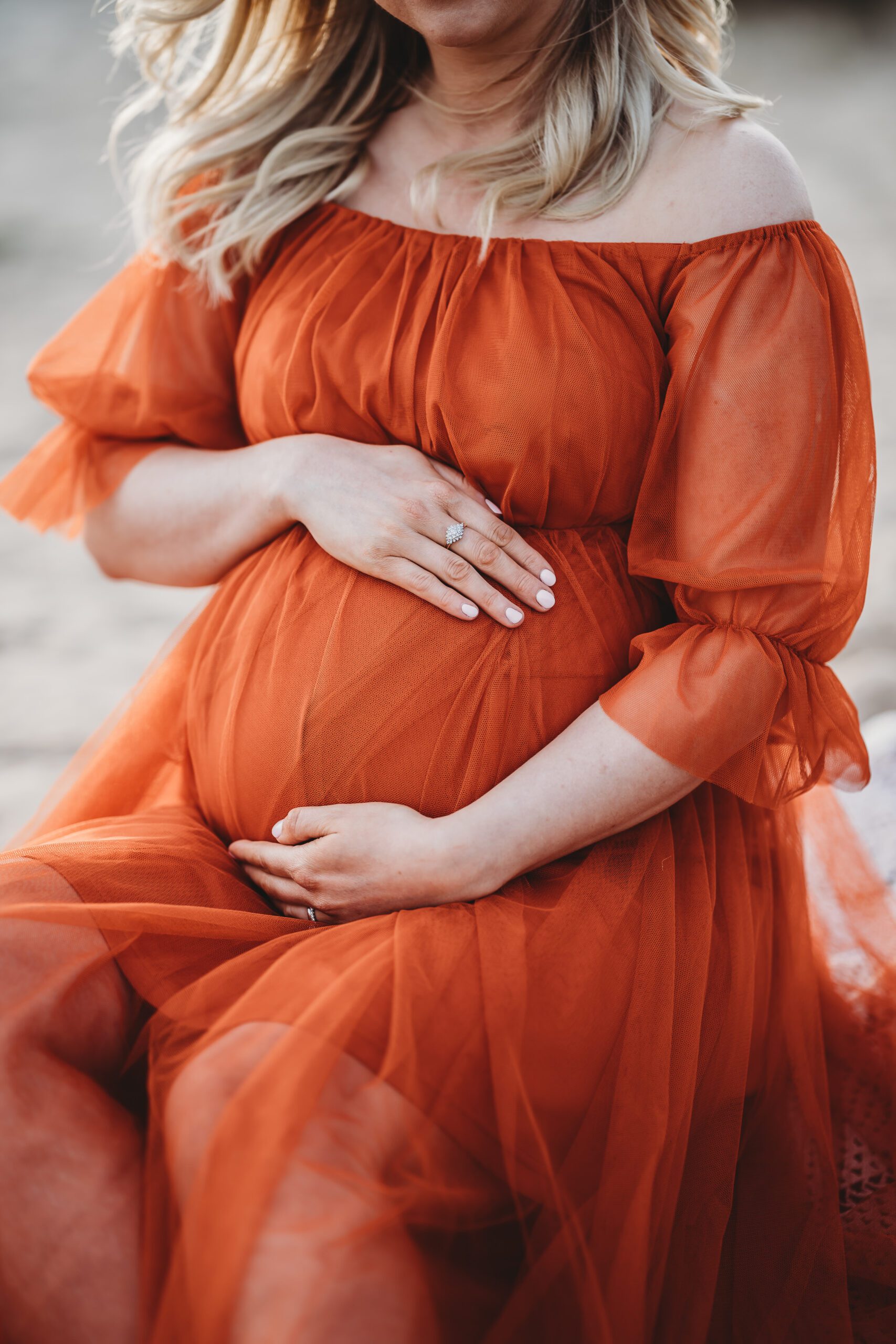 a close up image of a pregnant lady holding on to her bump in a bright orange dress taken by a newbury maternity photographer