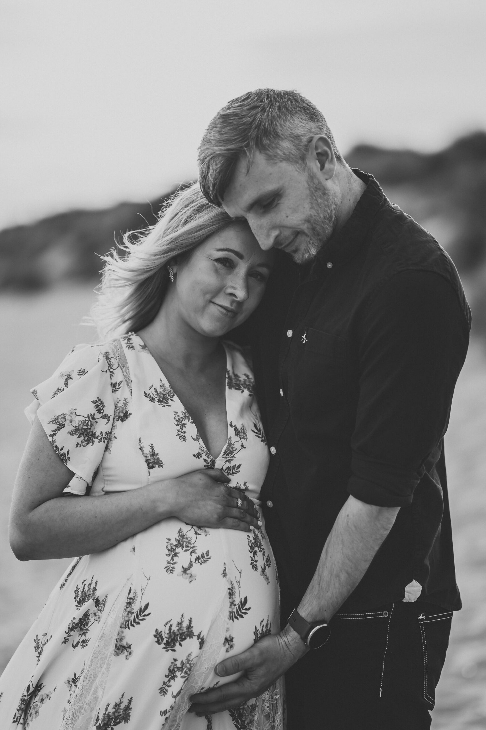 a soon-to-be dad cuddling his pregnant wife on a south coast beach for a newbury maternity photographer