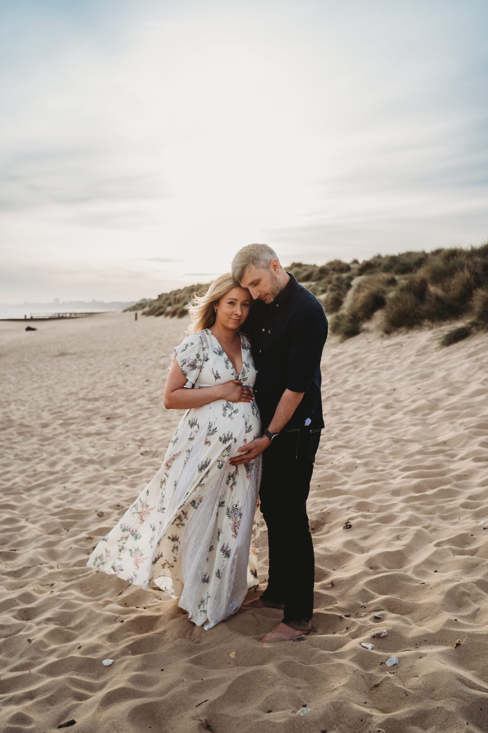 a soon-to-be dad cuddling his pregnant wife on a south coast beach for a newbury maternity photographer