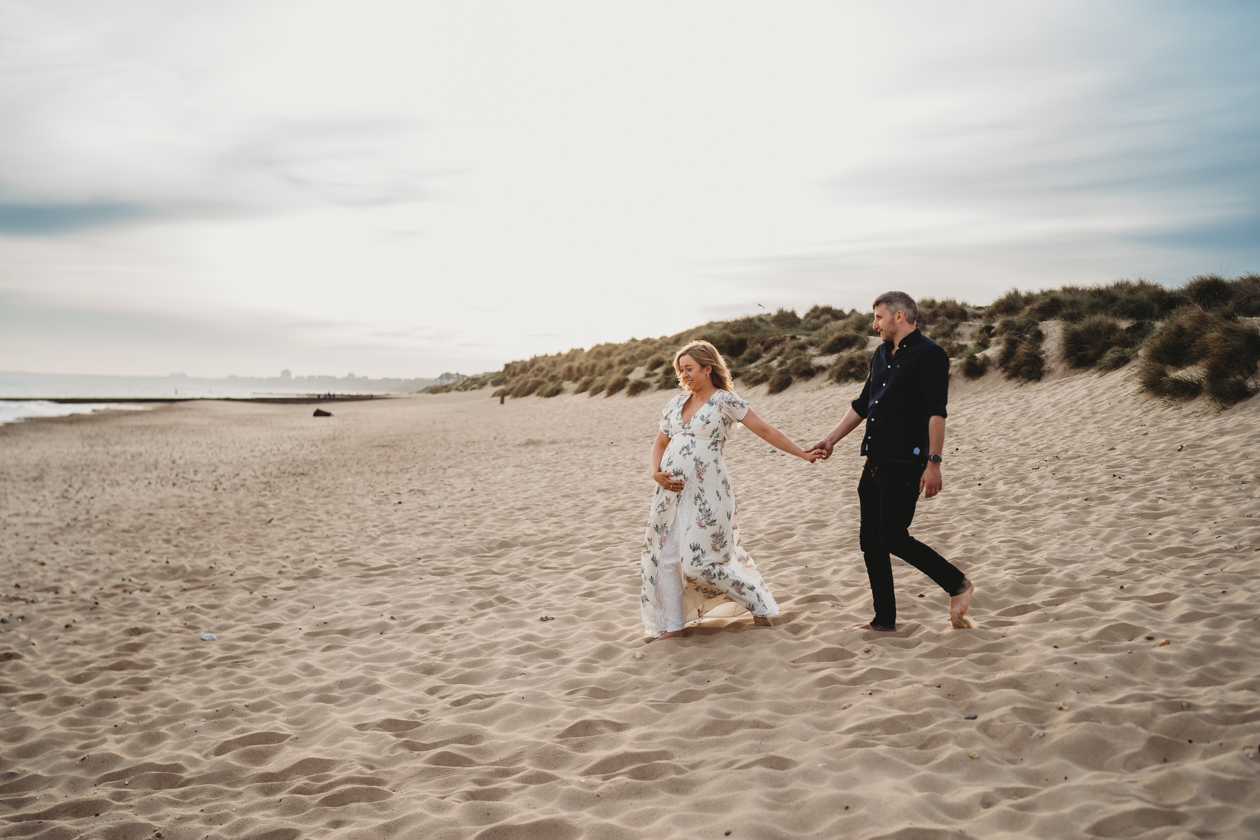 a pregnant lady leading her husband towards the sea for a newbury Materniry photographer