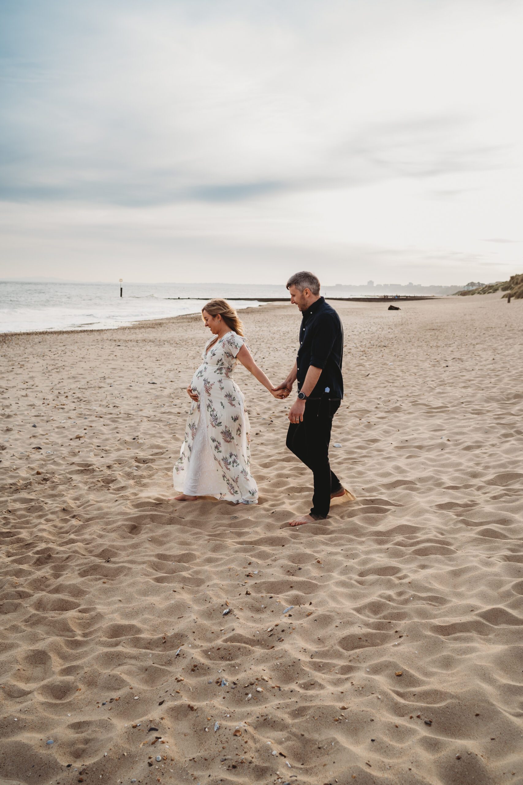 a pregnant lady leading her husband towards the sea for a newbury Materniry photographer