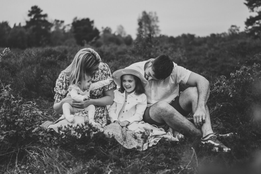 a black and white photo of a family of 4 sat down laughing and chatting for a summer family photoshoot in Newbury