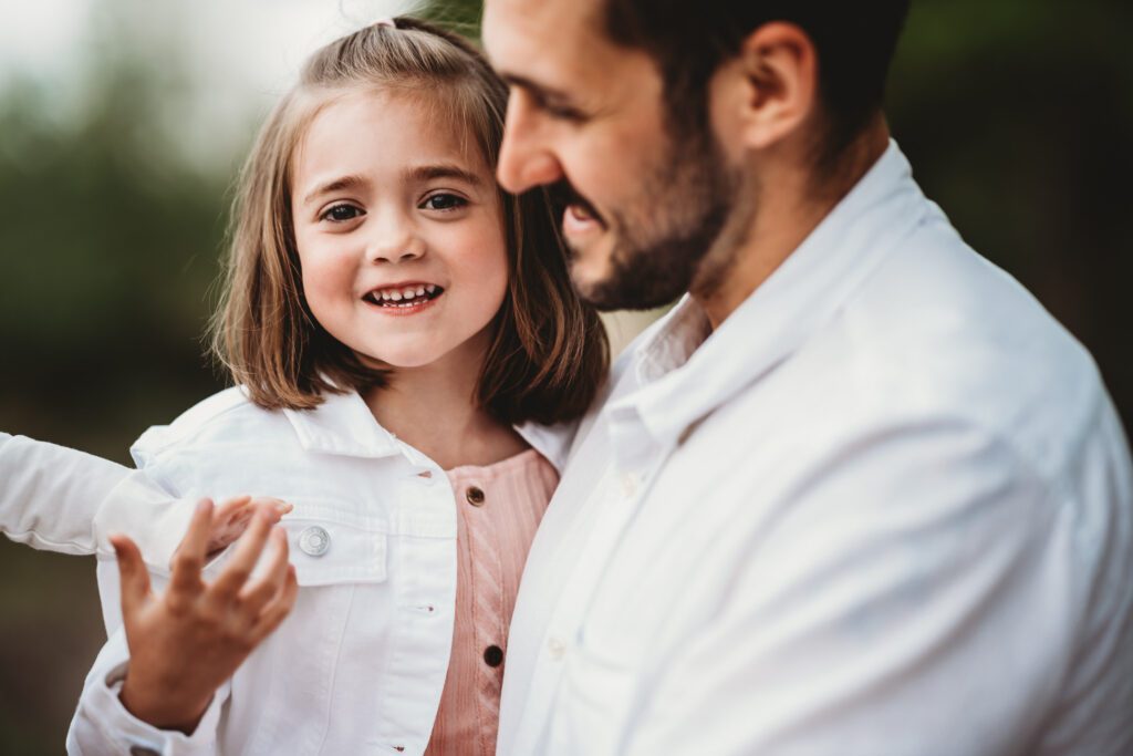 a little girl smiling at the camera whilst being held by her dad for a berkshire family photographer