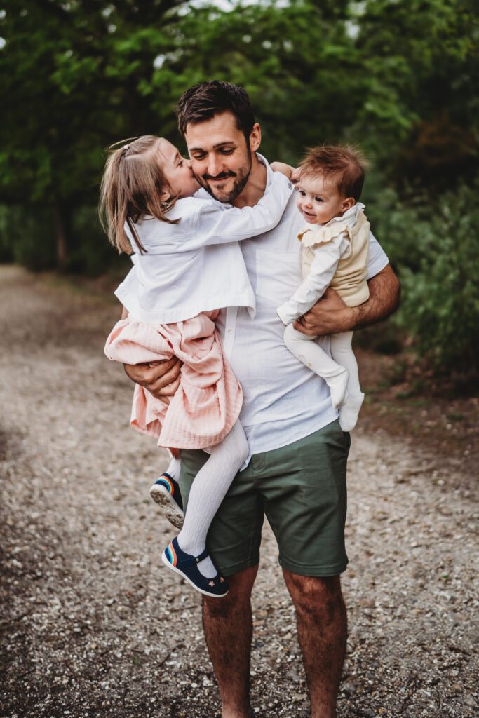 a dad picking up his 2 girls as he hugs them smiling, for a summer family photoshoot in Newbury