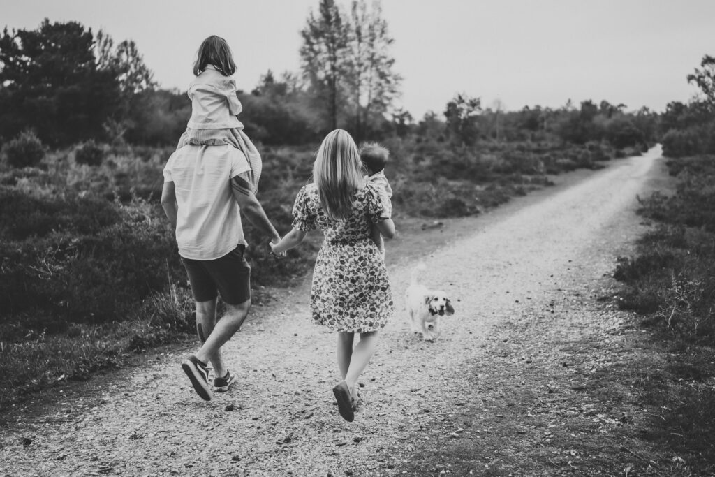 a black and white image of a family of 4 holding hands and walking away from the camera for a newbury Family Photographer