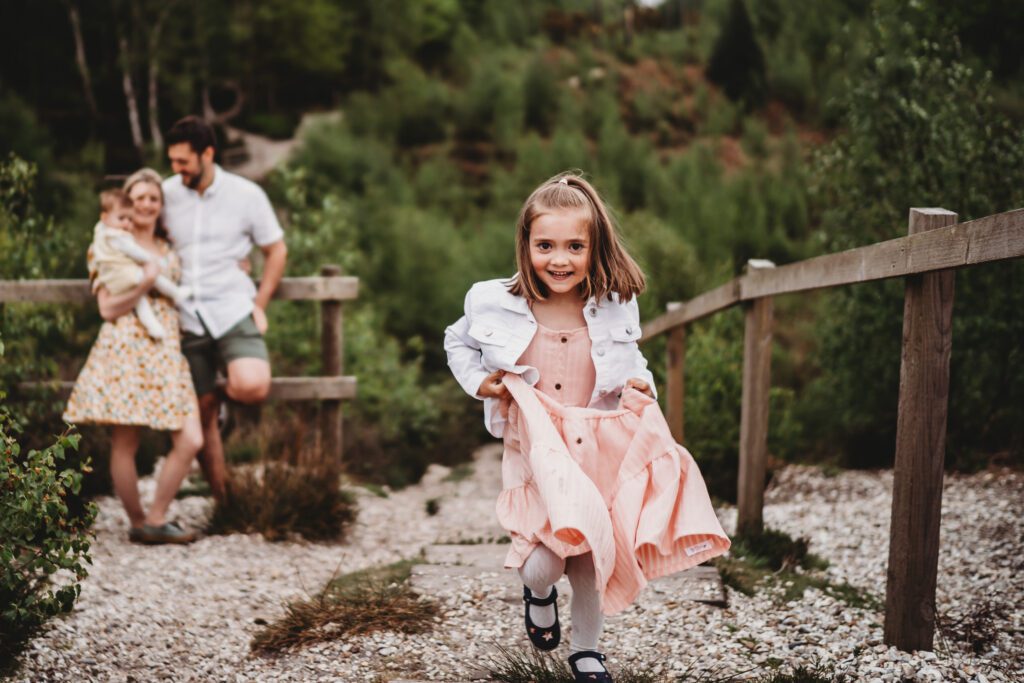 a little girl running towards the camera whilst her family watch on in the background