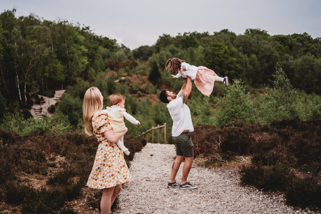 a mum and her daughter look on as the dad picks his little girl up in the air