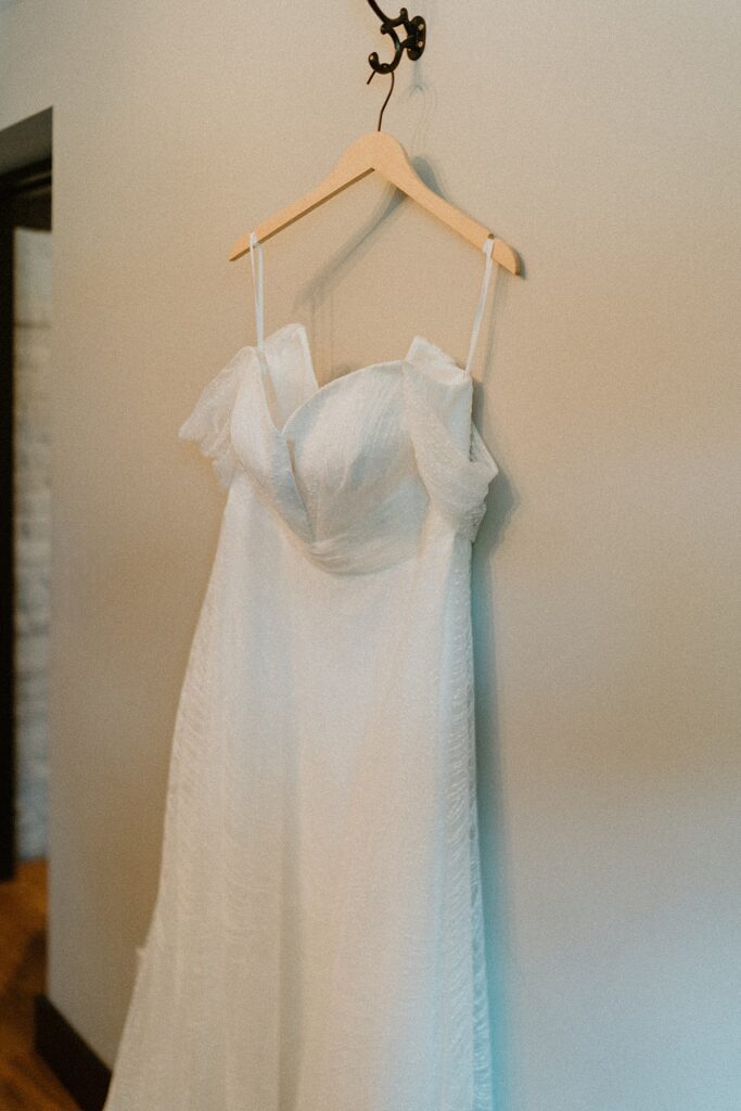 a dress hanging up against a cream wall during bridal prep