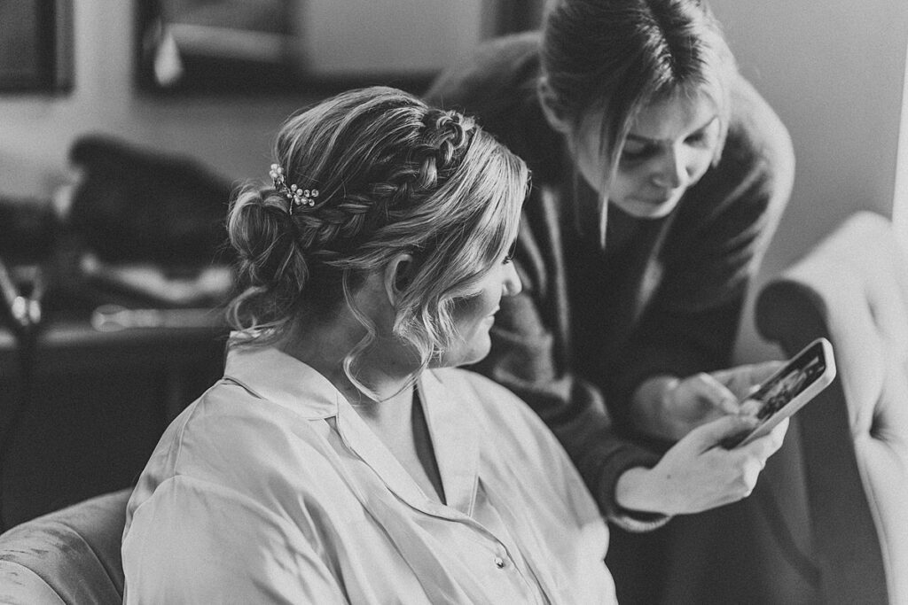 a hairdresser showing a bride a photo on her phone during bridal prep