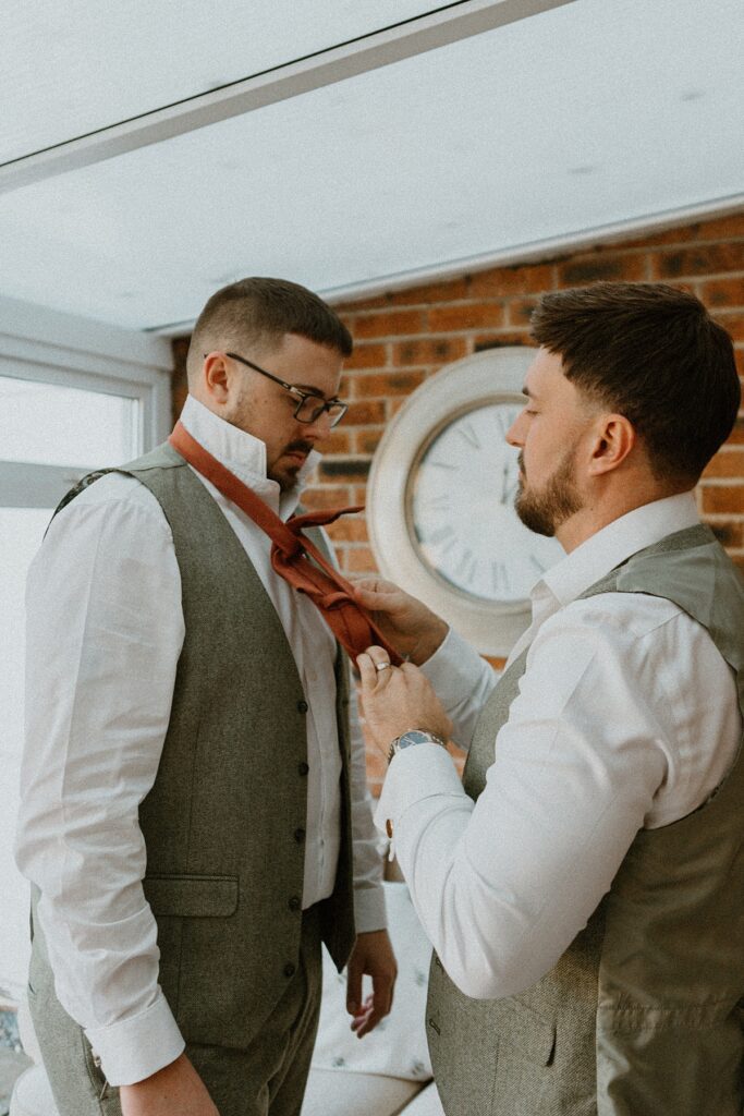 the bestman helping the groom with his tie during groom prep