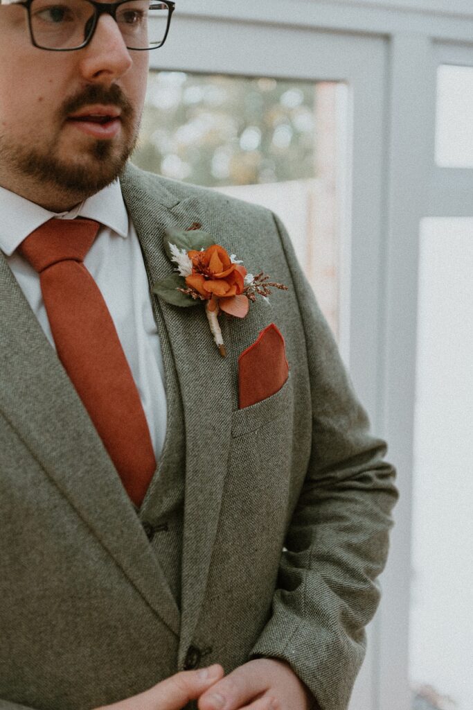 a close up of a grooms suit and button hole before his marriage at Ufton Court posing for a wedding photographer