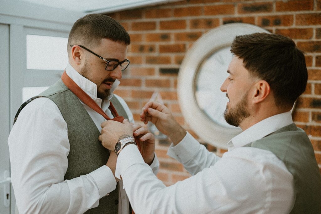 a groom being helped by his bestman to do his tie ready for his wedding