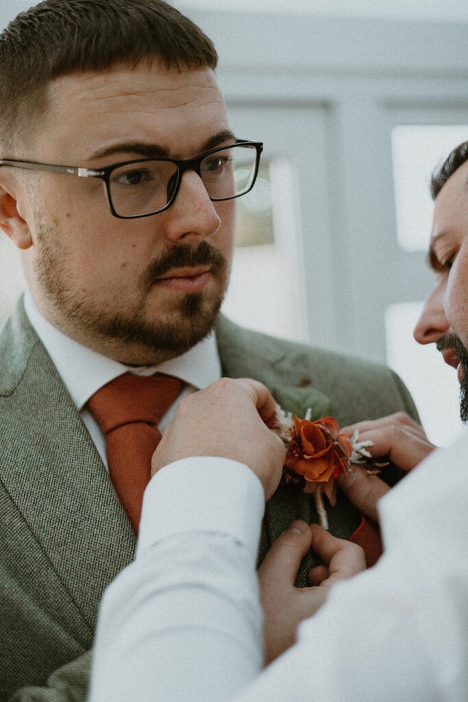 a groom being helped with his button hole before his marriage