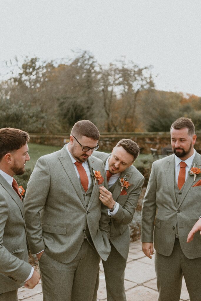 groomsmen fussing around a groom making sure him and his suit look ready for his wedding at Ufton Court