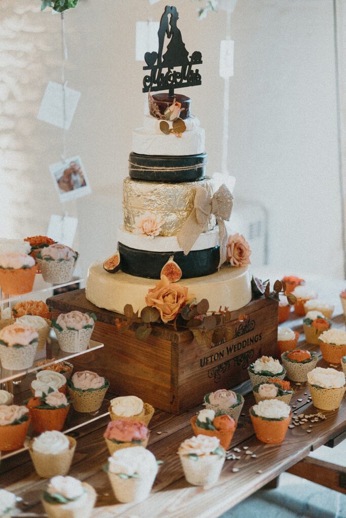 a wedding cake decorated in black and gold surrounded by smaller cup cakes