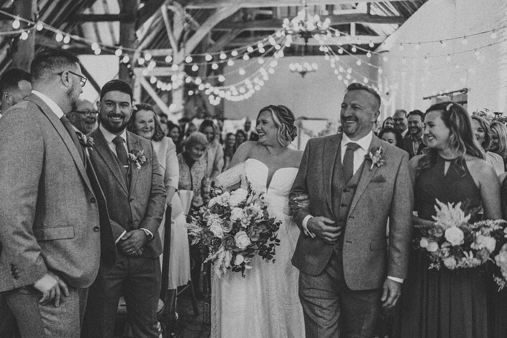 a black and white image of a a black and white image of a bride being walked down the aisle at Ufton Court