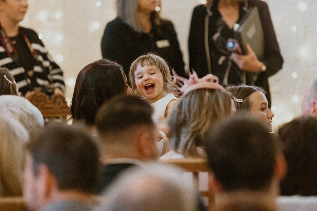 a flower girl laughing as she looks over her mums shoulder during a wedding service at Ufton Court