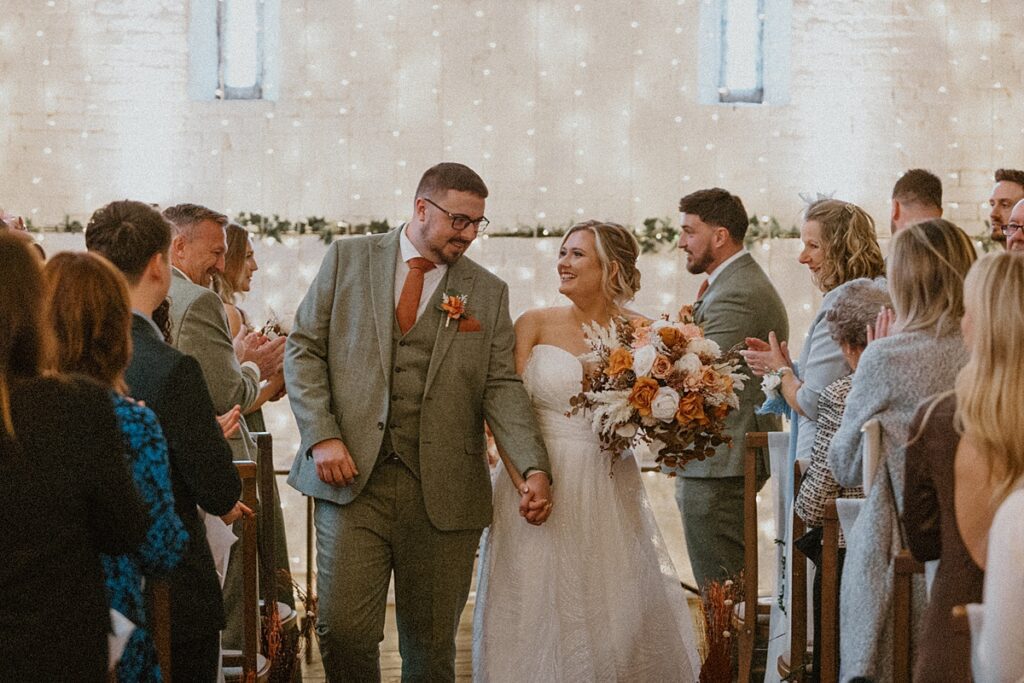 a bride and groom looking at each other as they walk back down the aisle at Ufton Court