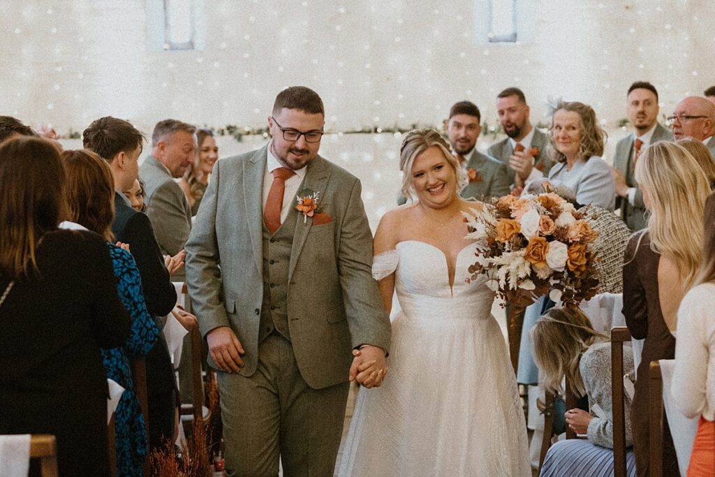 a bride and groom looking at each other as they walk back down the aisle at Ufton Court