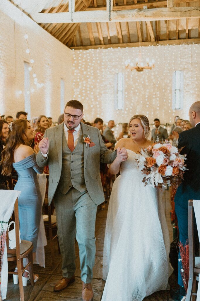 a bride and groom looking at each other as they walk back down the aisle at Ufton Court