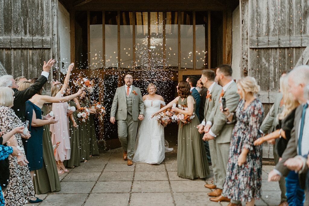 a bride and groom walking down a confetti line up outside the barn at Ufton Court in Newbury