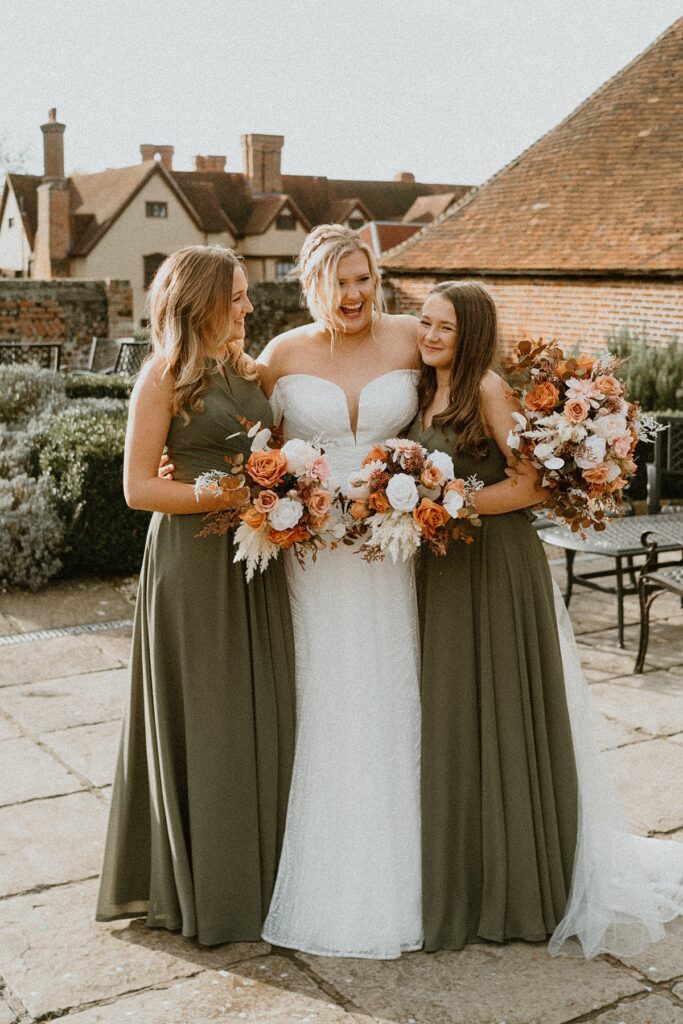 a bride hugging on to her two bridesmaid sisters and laughing during her wedding day