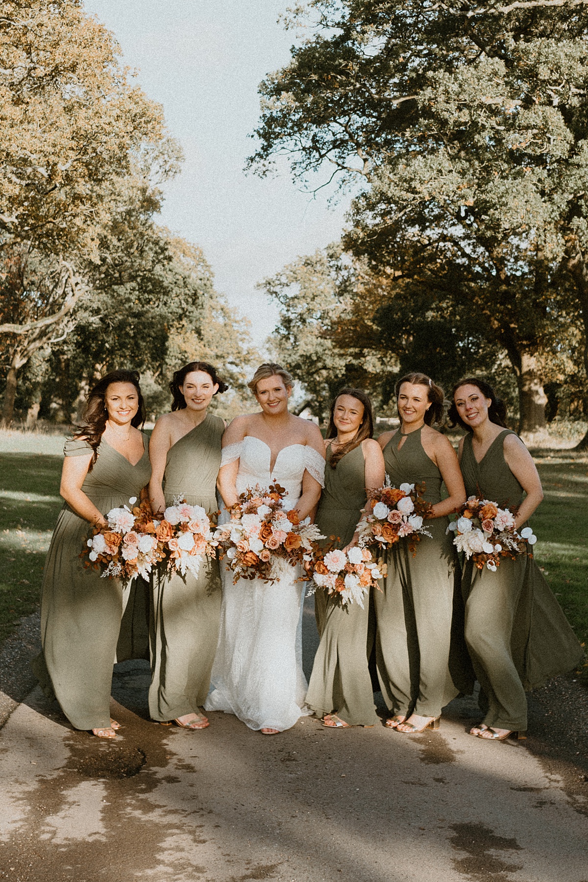 a line up of bridesmaids dressed in khaki green dresses, leaning into each other on the driveway at Ufton Court