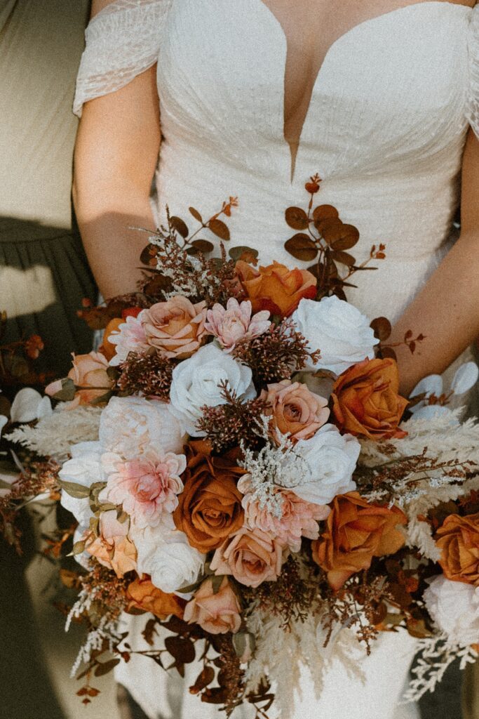 a close up of a brides bouquet with brown, orange, white and cream flowers