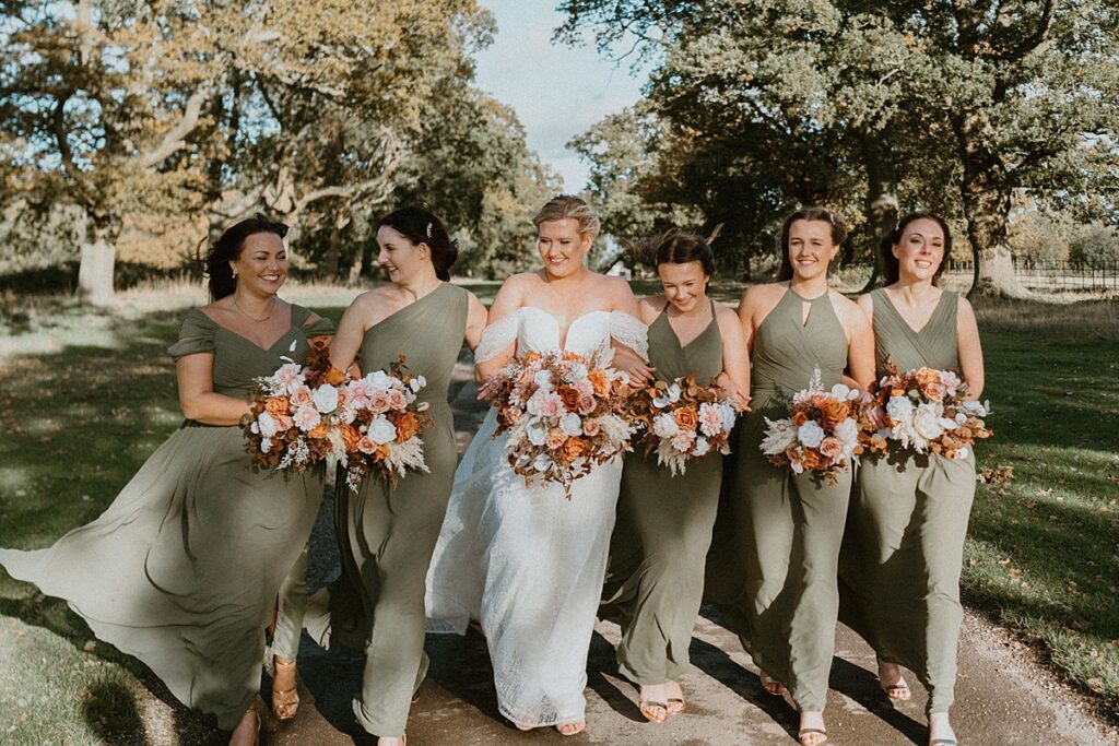 a line up of a bride with her bridesmaids dressed in khaki green dresses, walking and talking to each other