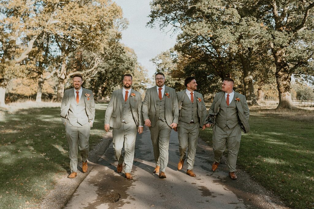 a line up of groomsmen walking and talking down the driveway of Ufton Court