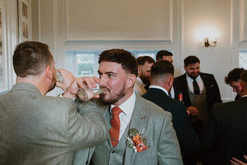 2 groomsmen linking arms and drink their drinks at a wedding reception at Ufton Court