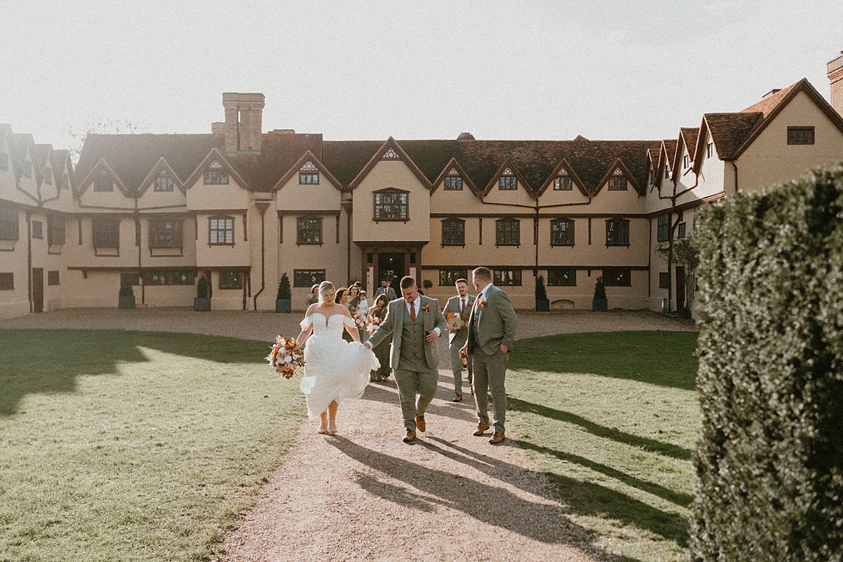 a wedding party walking towards a luxury wedding photographer with Ufton Court behind them