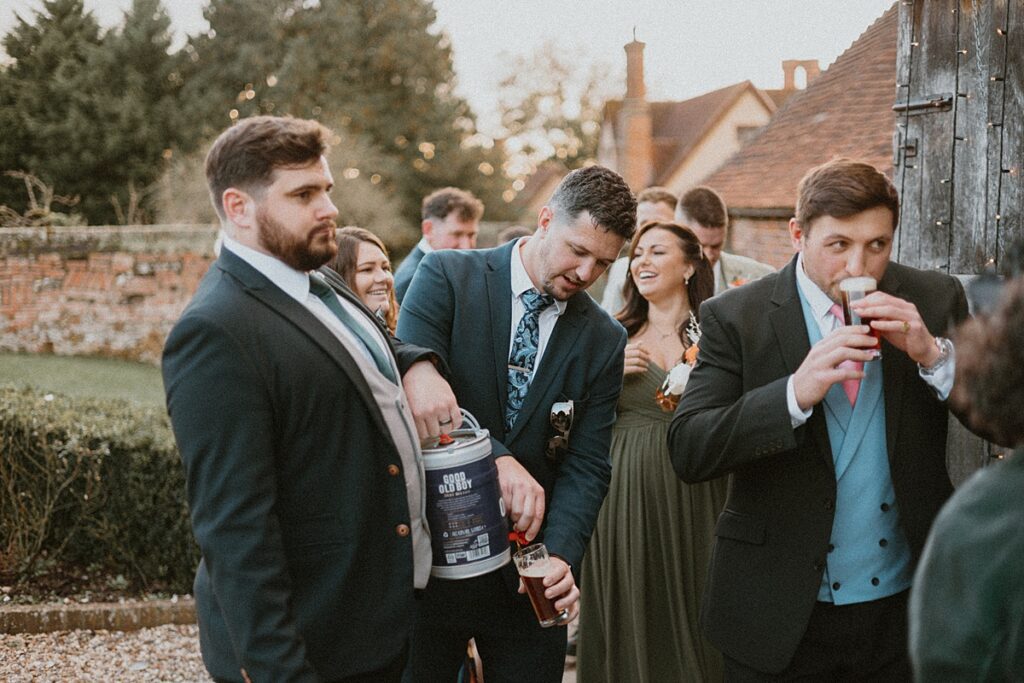 a guest helping himself to a beer from a keg being held by another wedding guest