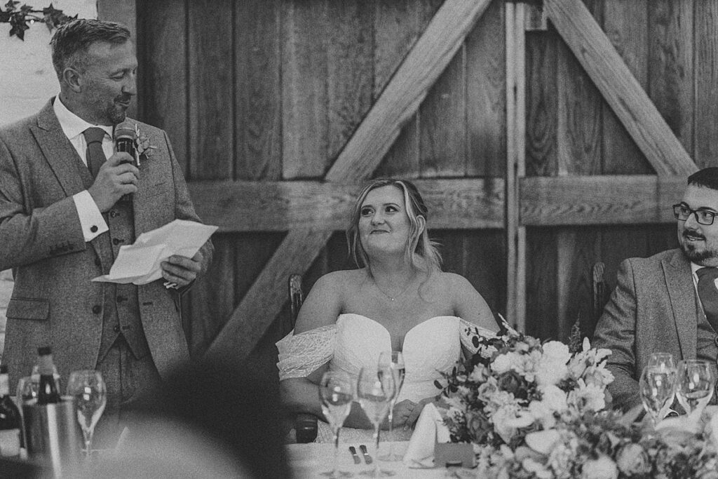 a bride smiling at her dad reads his father of the bride speech