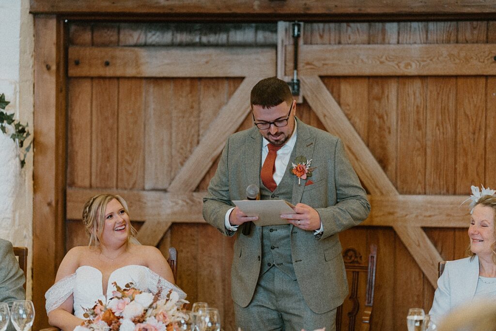 a groom reading his speeche as his new wife smiles on at Ufton Court Barn